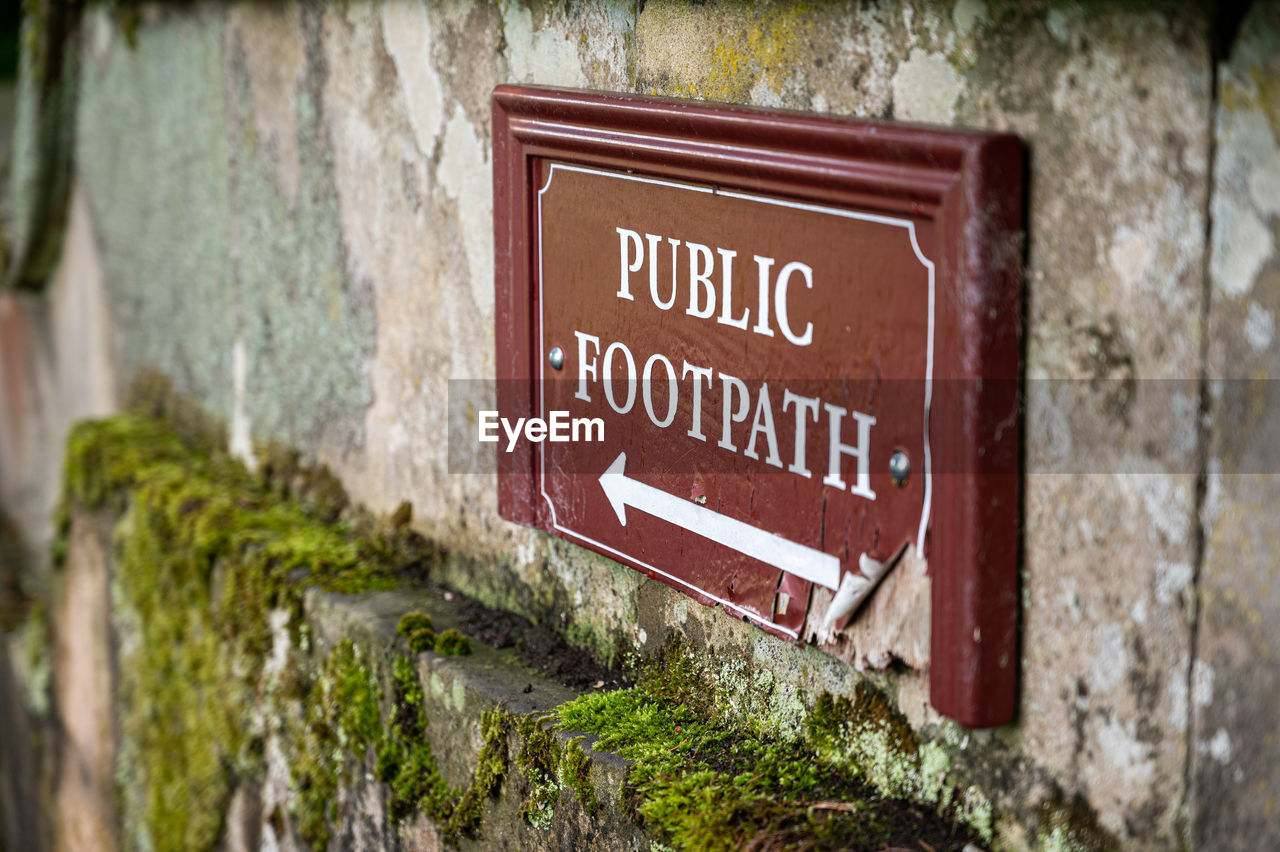An old distressed public footpath sign on a moss covered old stone wall.