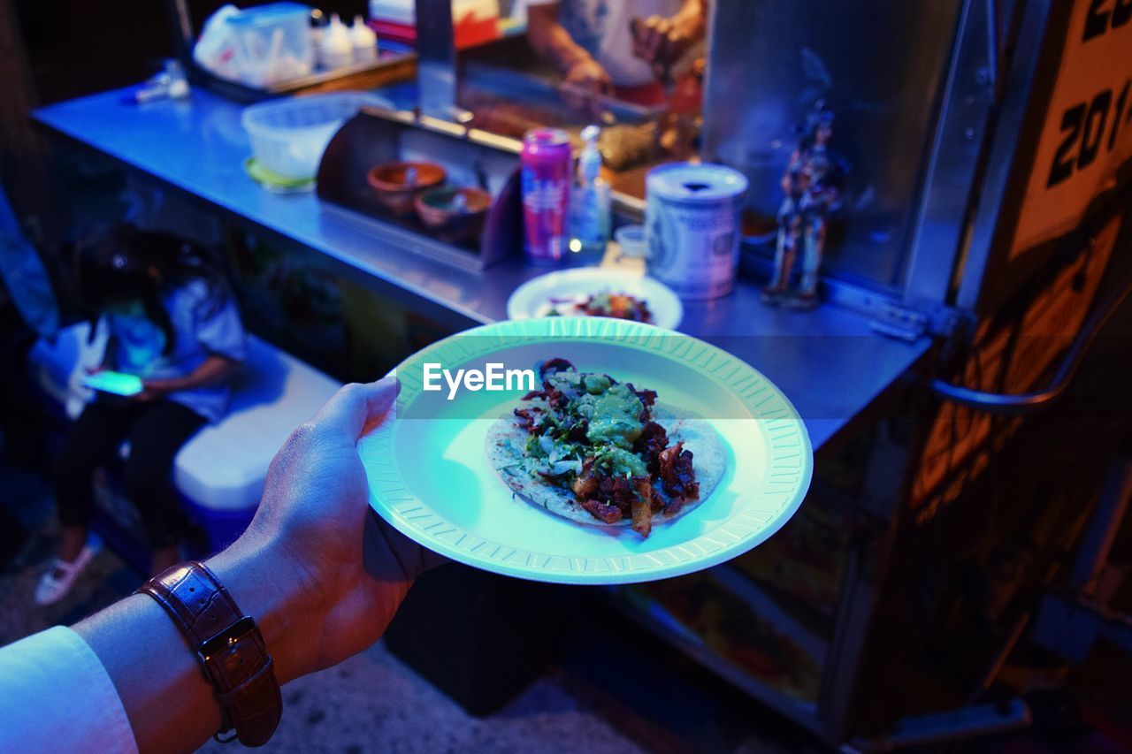 Cropped image of man holding taco in plate at food stall