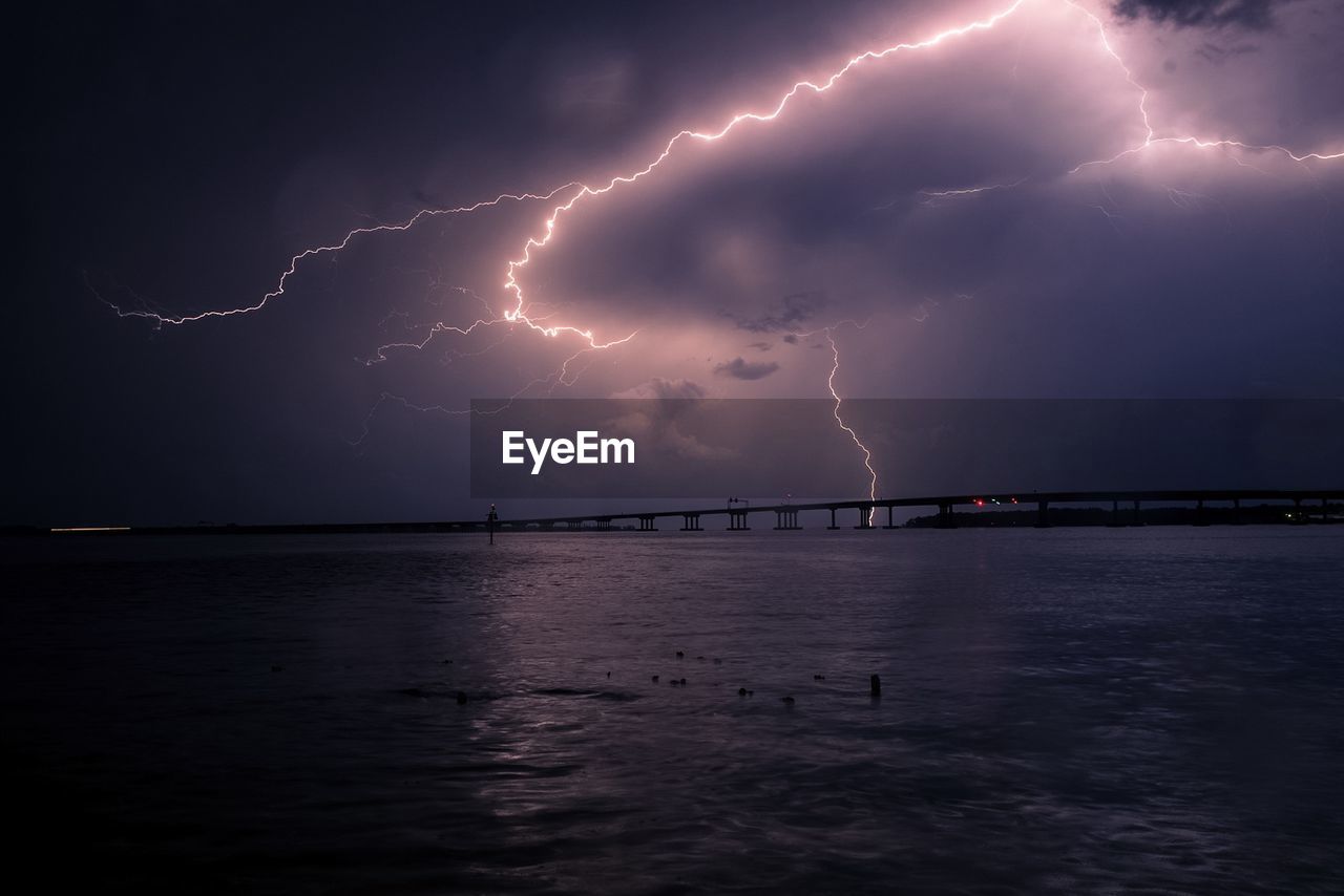Low angle view of lightning on silhouette pier over sea during dusk