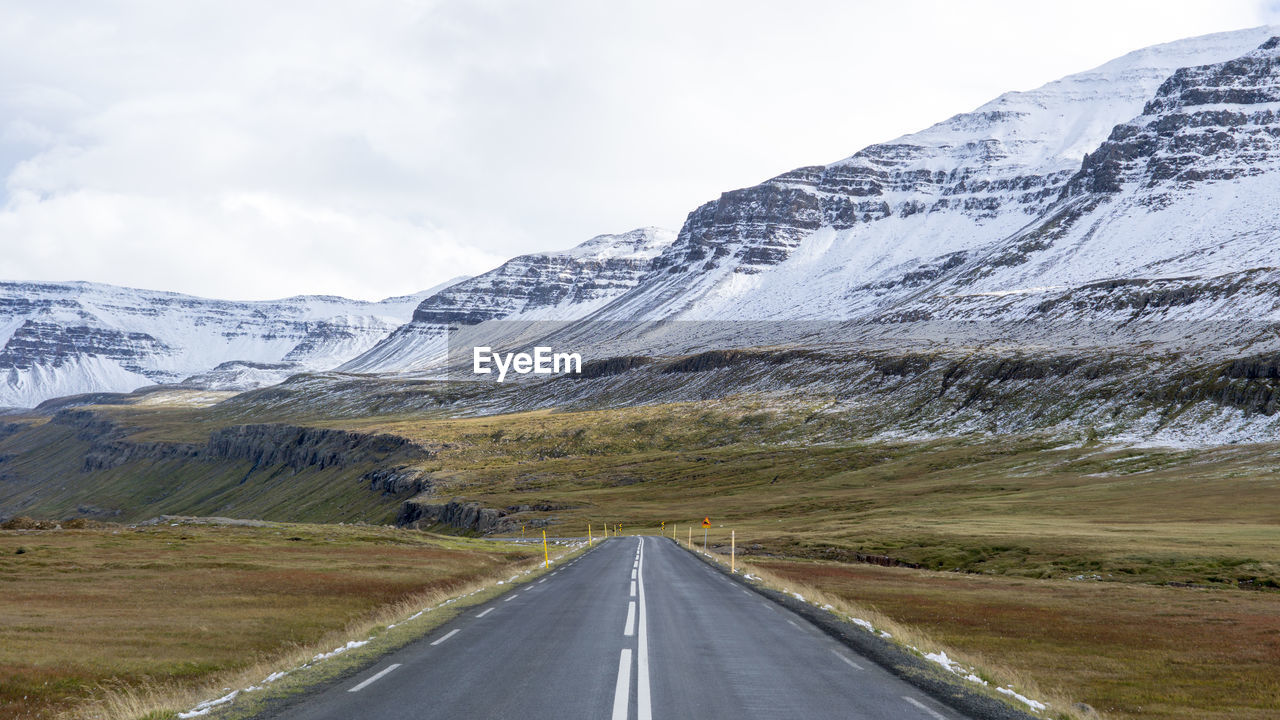 Road leading towards snowcapped mountains against sky