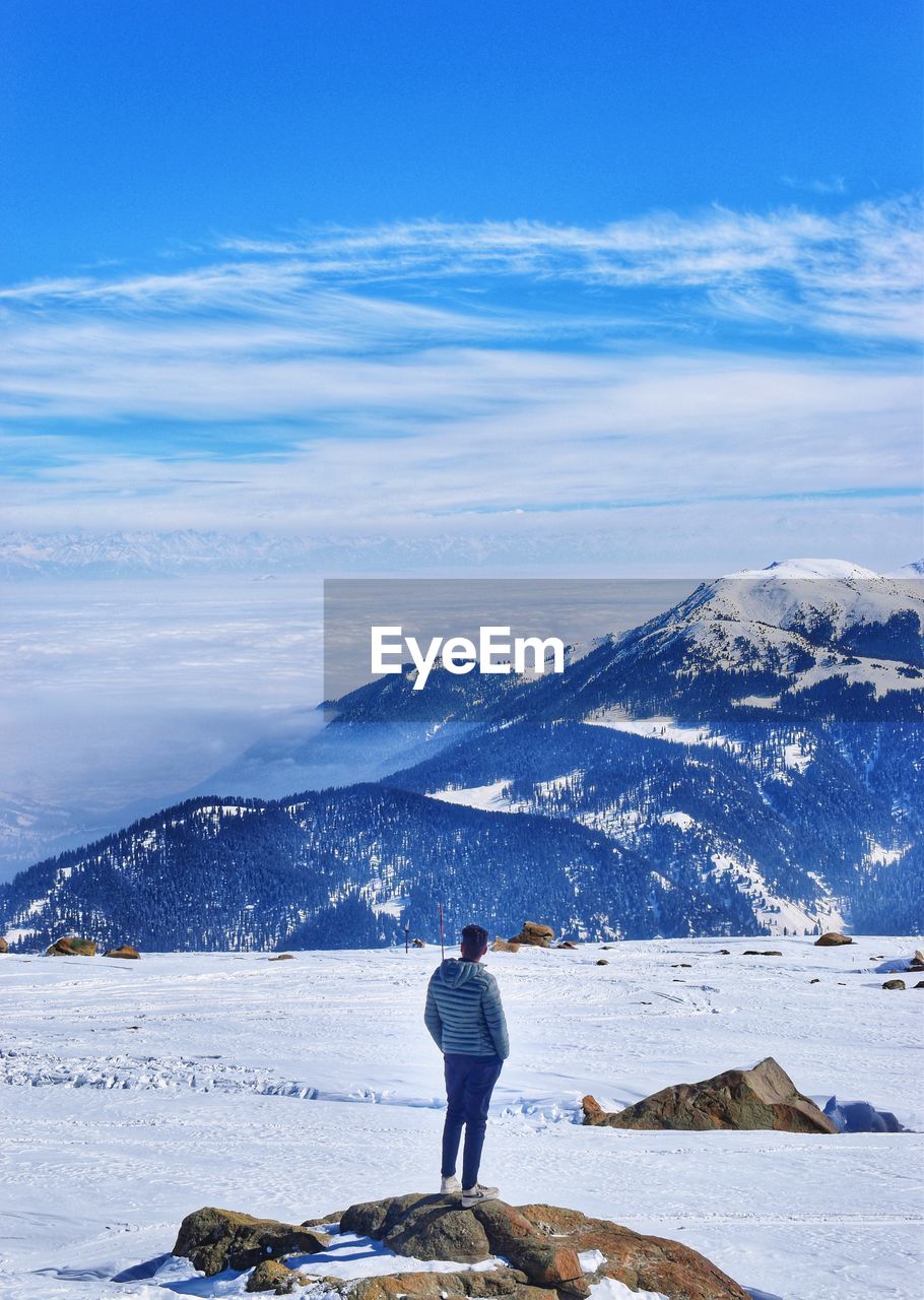 Rear view of woman standing on snowcapped mountain against blue sky