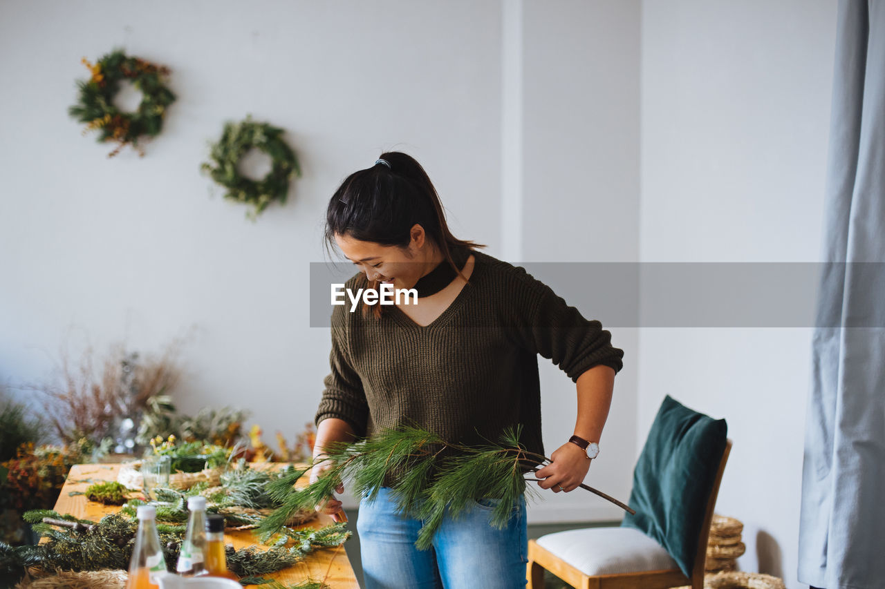 Young woman holding plant decorations at home during christmas