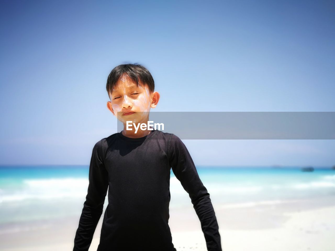 Boy standing on shore at beach against sky during sunny day