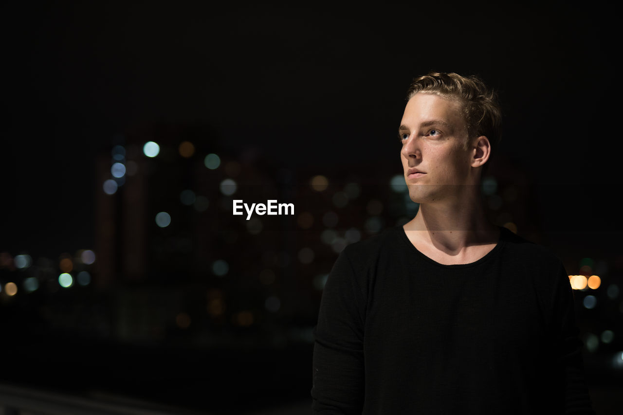 PORTRAIT OF YOUNG MAN STANDING AT NIGHT