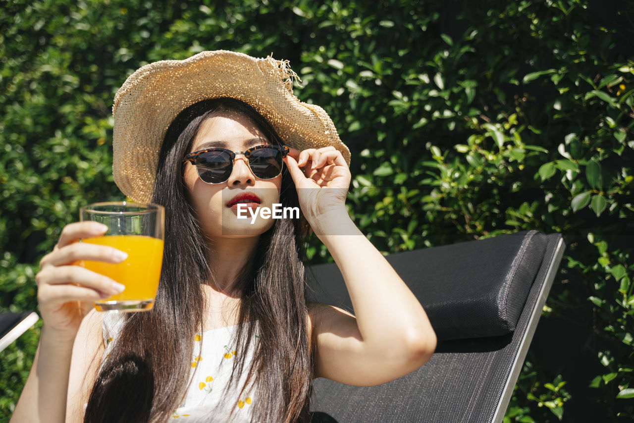 Portrait of young woman holding juice while sitting outdoors