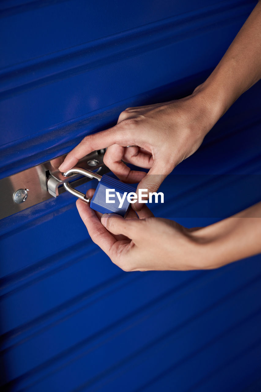 Anonymous cropped woman hands holding a blue padlock while closing it