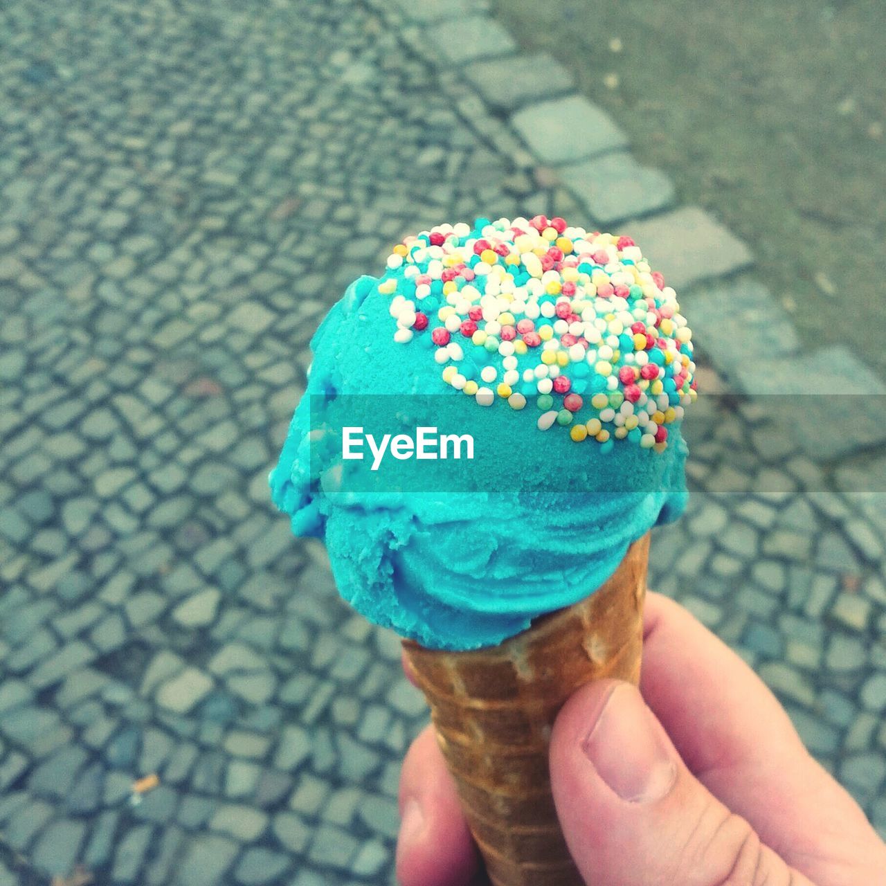 Person holding blue ice cream against cobblestone street
