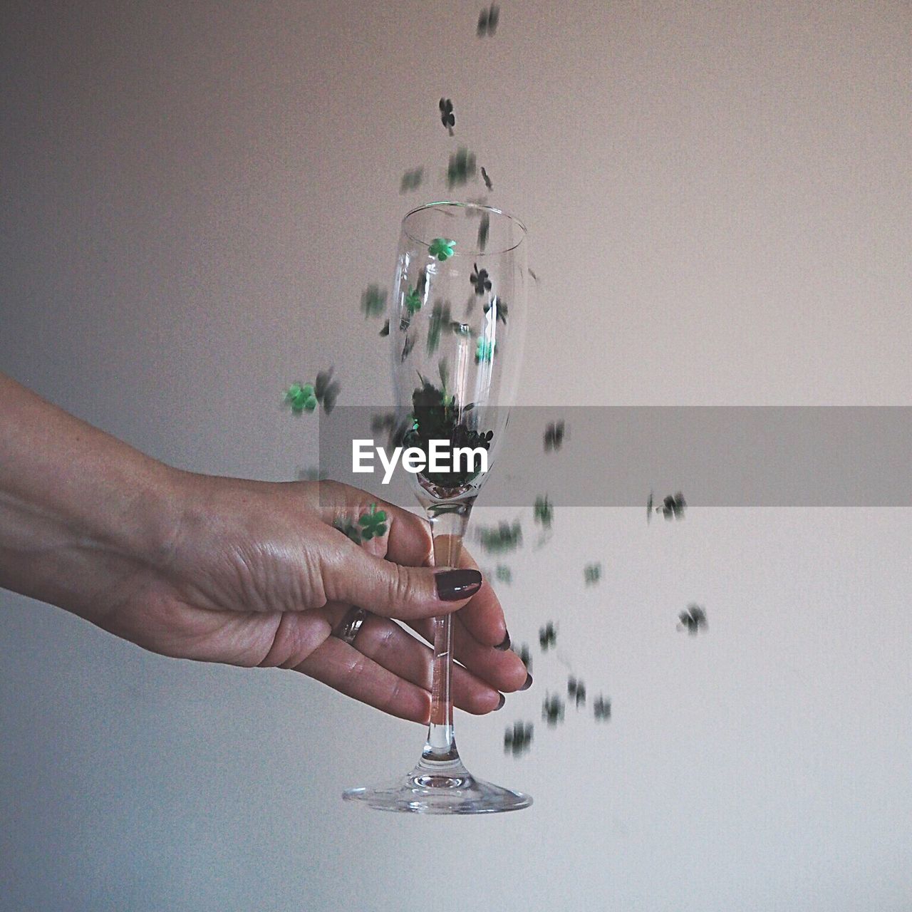Close-up of hand holding falling decorations in wineglass against wall