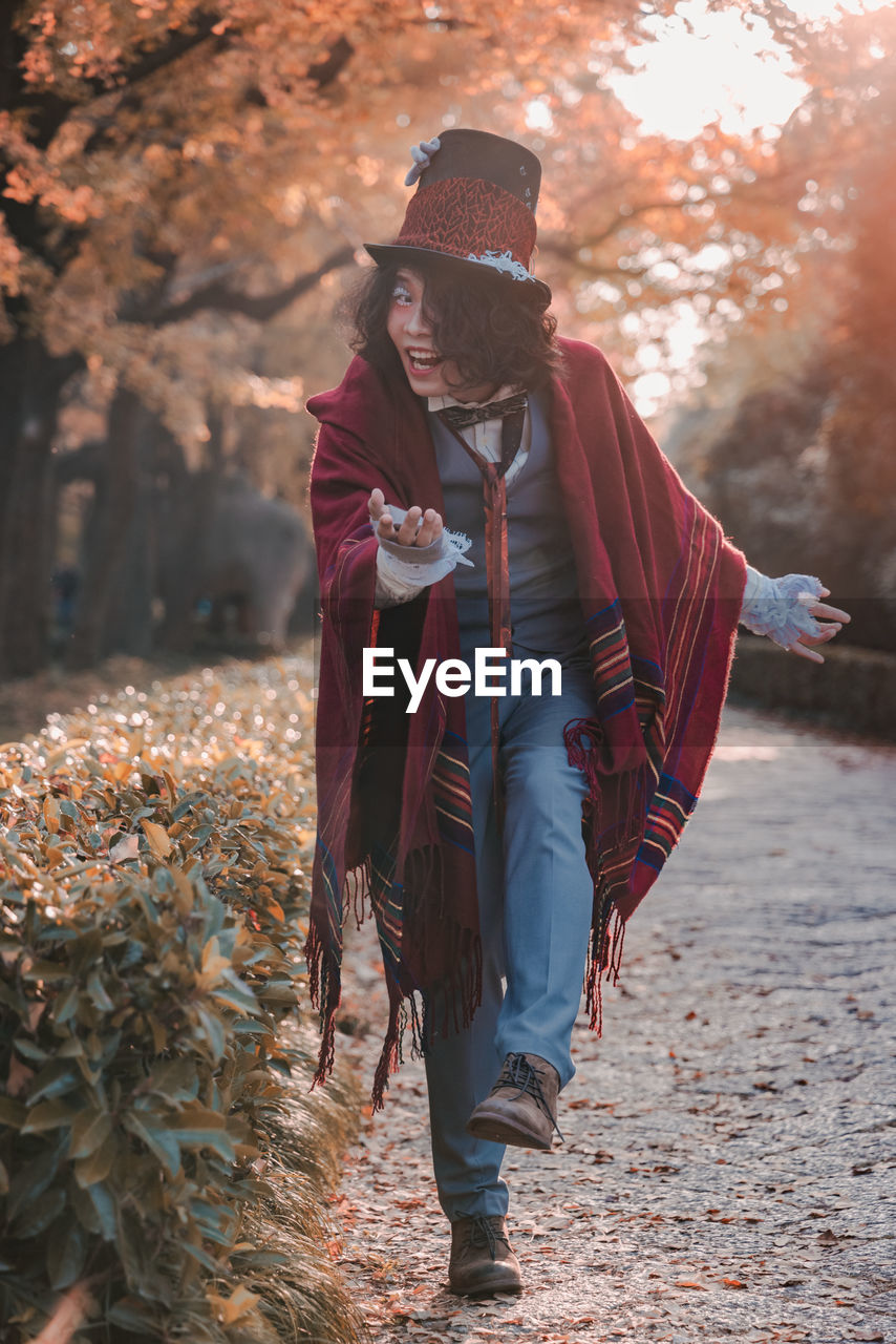 Man cosplaying mad hatter bowing on path next to hedges in autumn