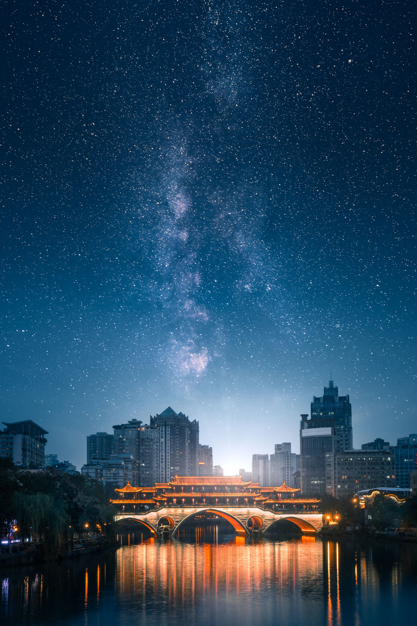 Illuminated bridge over river with buildings in background against star field