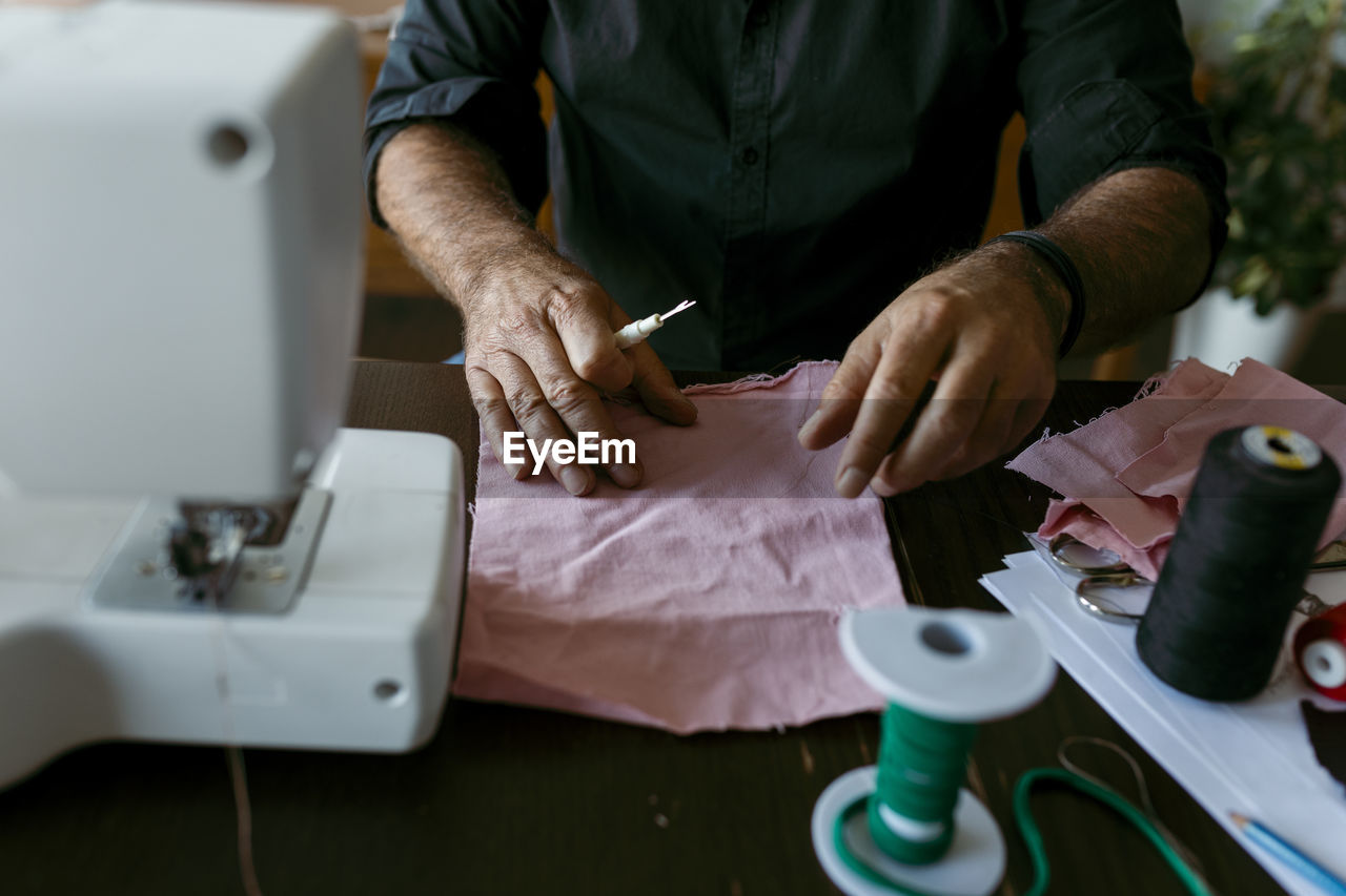 Mature male tailor with fabric working on table in work studio