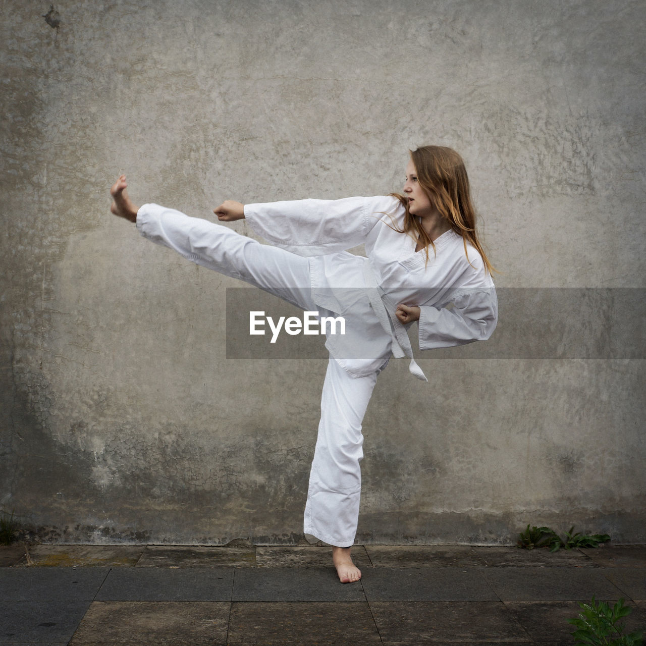 Young woman practicing karate against wall