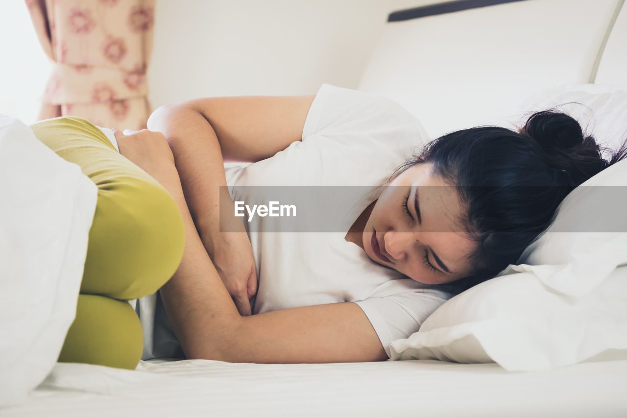 Woman with stomachache sleeping on bed