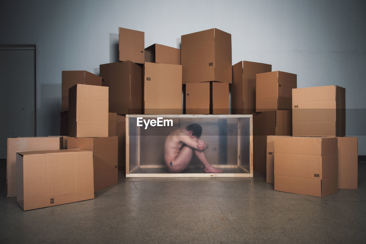Naked mid adult man sitting in container by cardboard boxes at home