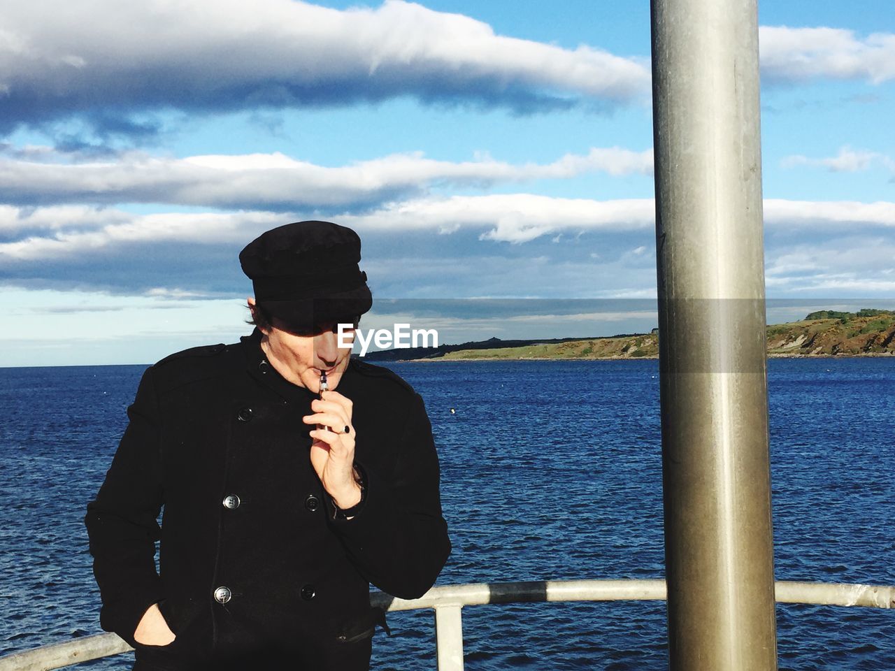 Man smoking by sea against sky