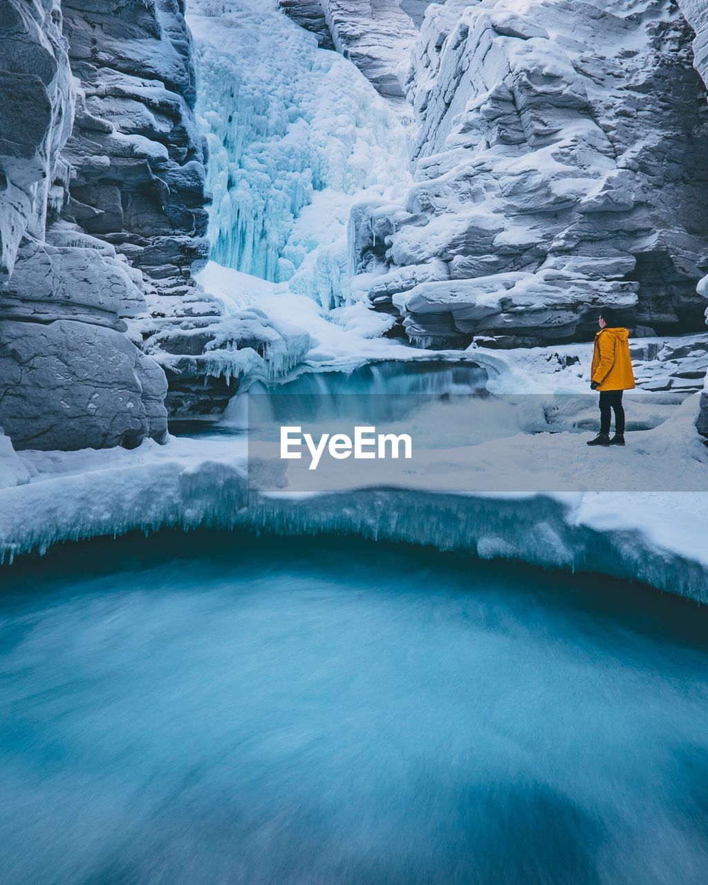 Side view of young man standing by frozen waterfall