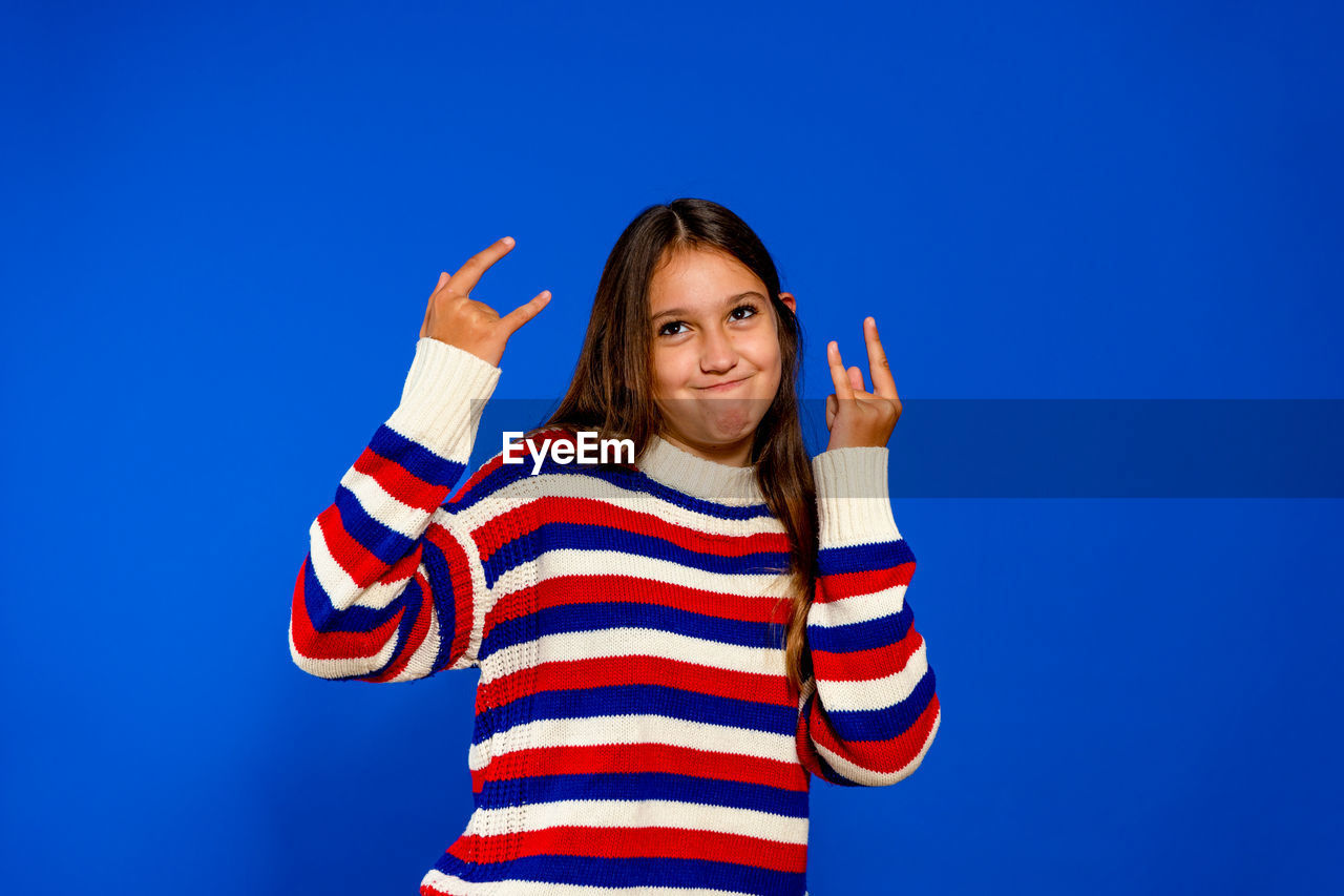 blue, striped, one person, studio shot, happiness, smiling, portrait, colored background, looking at camera, emotion, waist up, women, cheerful, blue background, copy space, front view, casual clothing, child, gesturing, person, fun, arm, adult, young adult, indoors, childhood, positive emotion, finger, standing, clothing, hand, limb, hairstyle, brown hair, human limb, lifestyles, joy, cut out