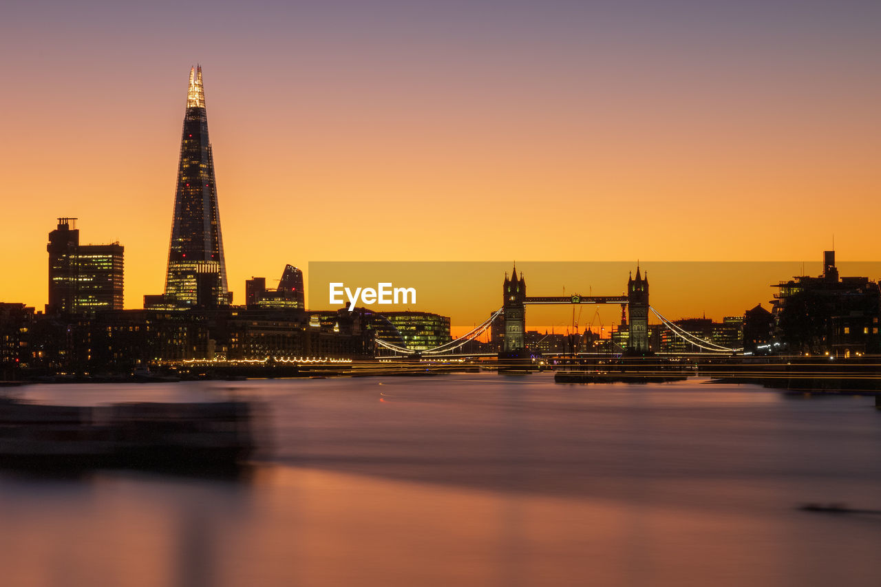 River in city against sky during sunset