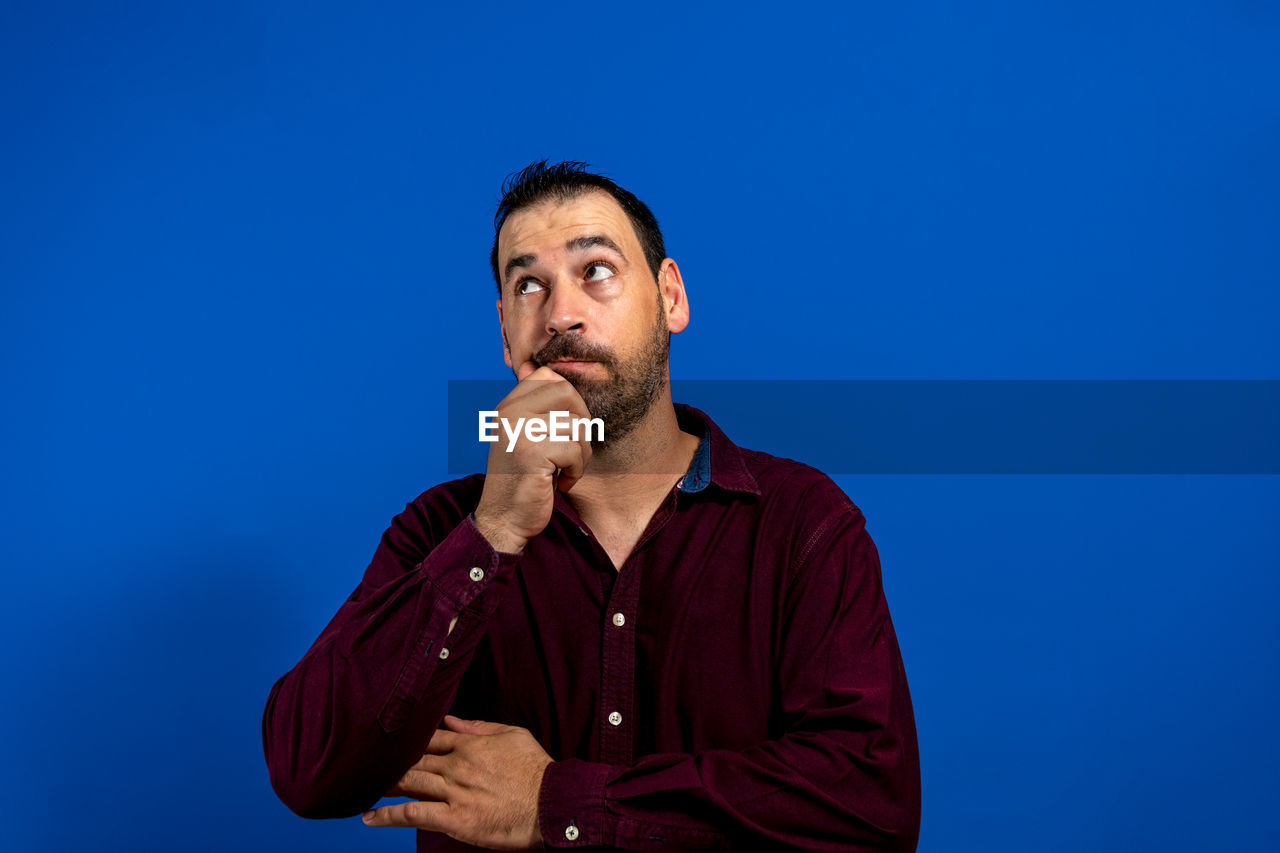 blue, one person, adult, men, blue background, portrait, studio shot, colored background, copy space, beard, facial hair, waist up, person, looking, casual clothing, front view, singing, contemplation, looking away, indoors, emotion, serious, speech, standing, button down shirt, sky, orator, young adult