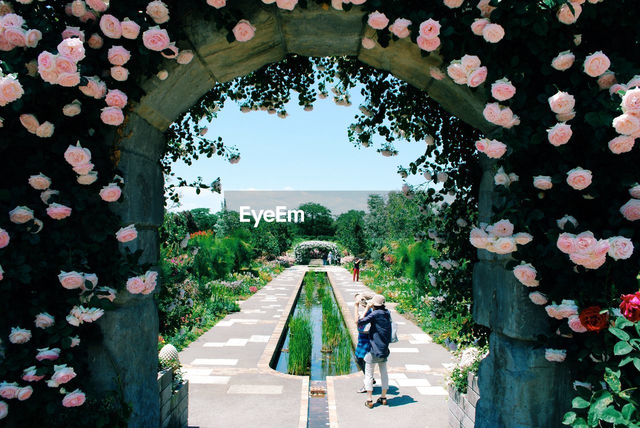 Women standing on footpath in garden seen through archway