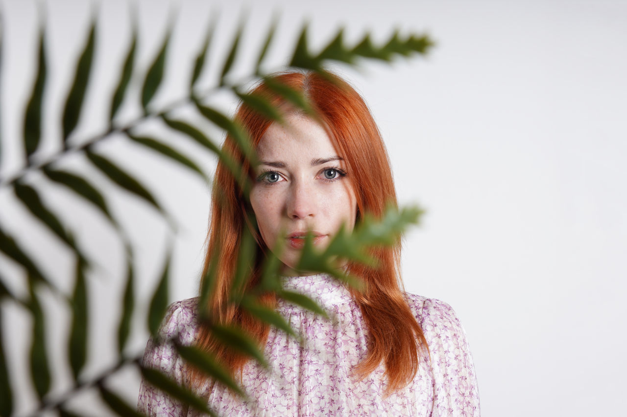 Mid adult woman hiding behind house plant palm leaves
