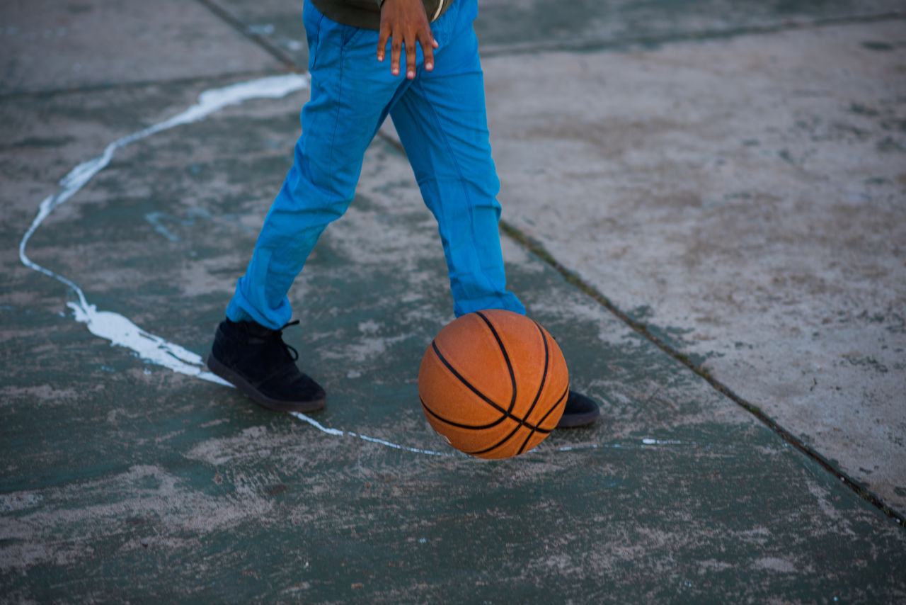 Low section of man playing basketball on footpath