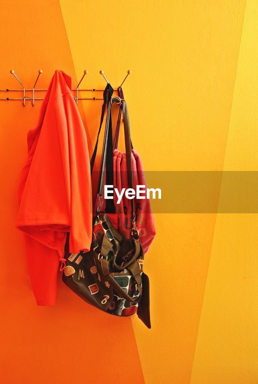 Clothes and shoulder bag hanging on yellow wall at home