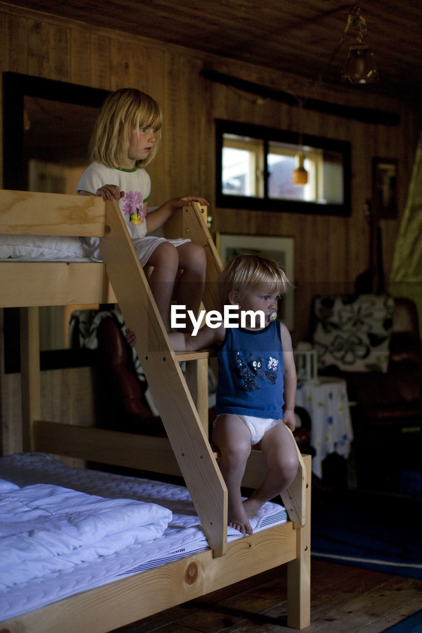 Brother and sister sitting on steps of bunkbed at home