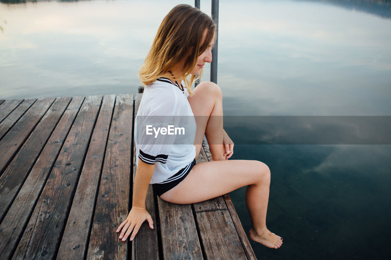 Young woman sitting on pier by lake