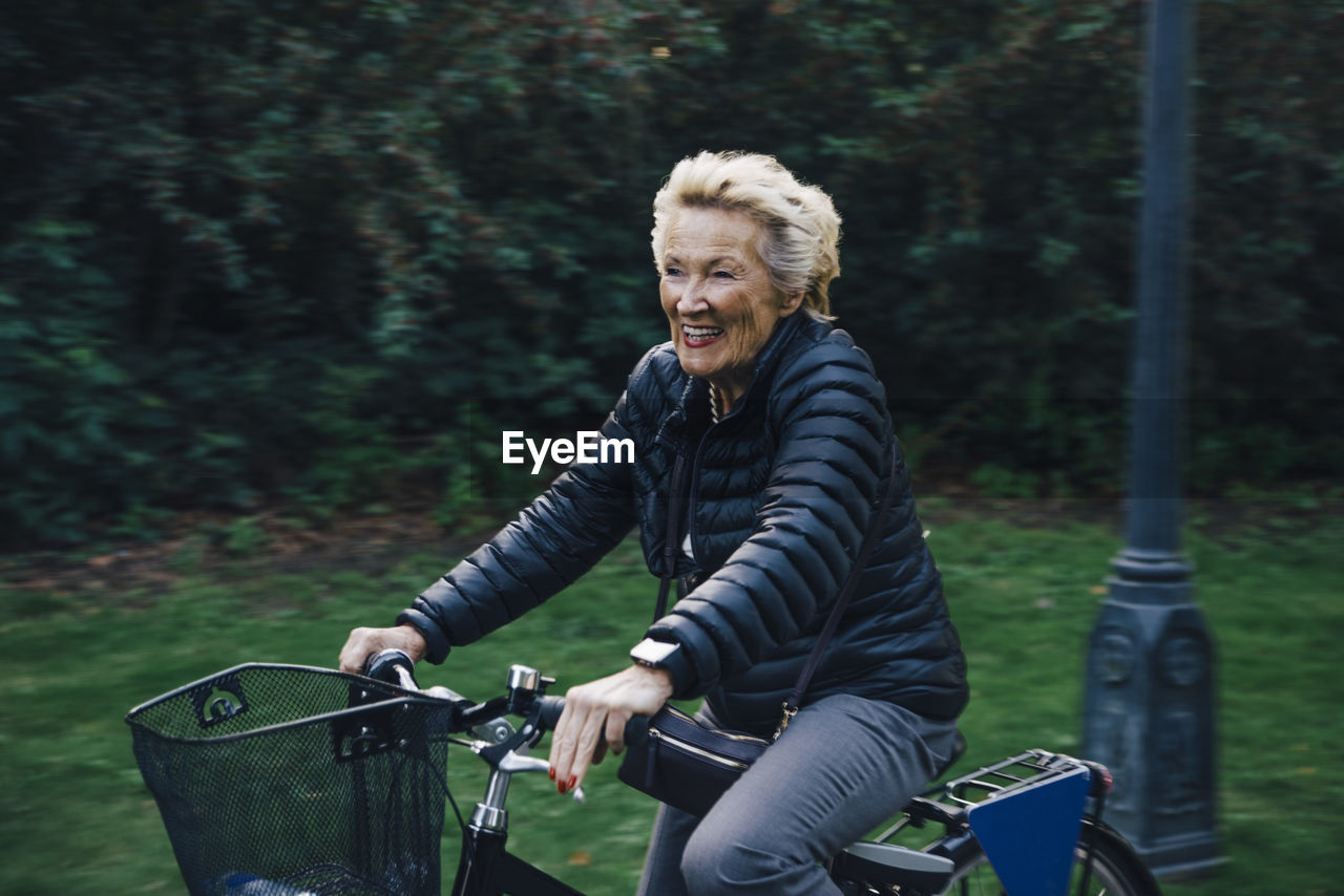 Smiling senior woman riding bicycle in park