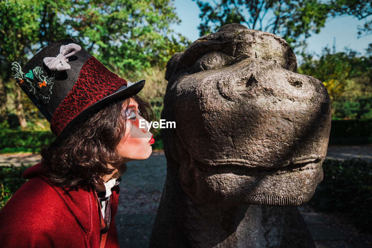 Portrait of man cosplaying mad hatter kissing statue