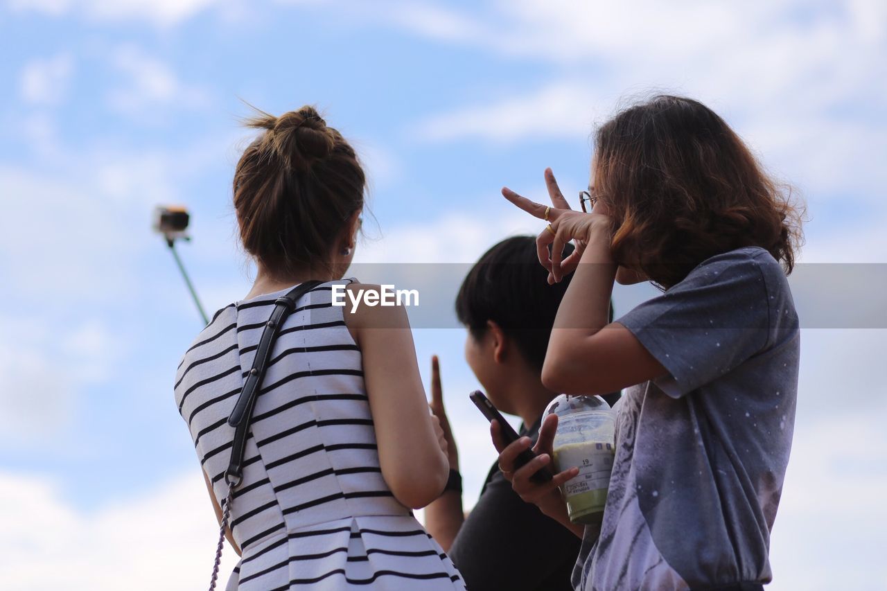 Woman taking selfie with friends against sky