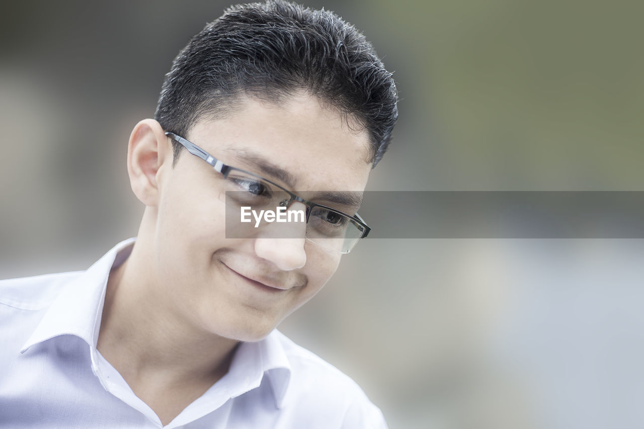 Close-up of smiling teenage boy wearing eyeglasses looking away while standing outdoors