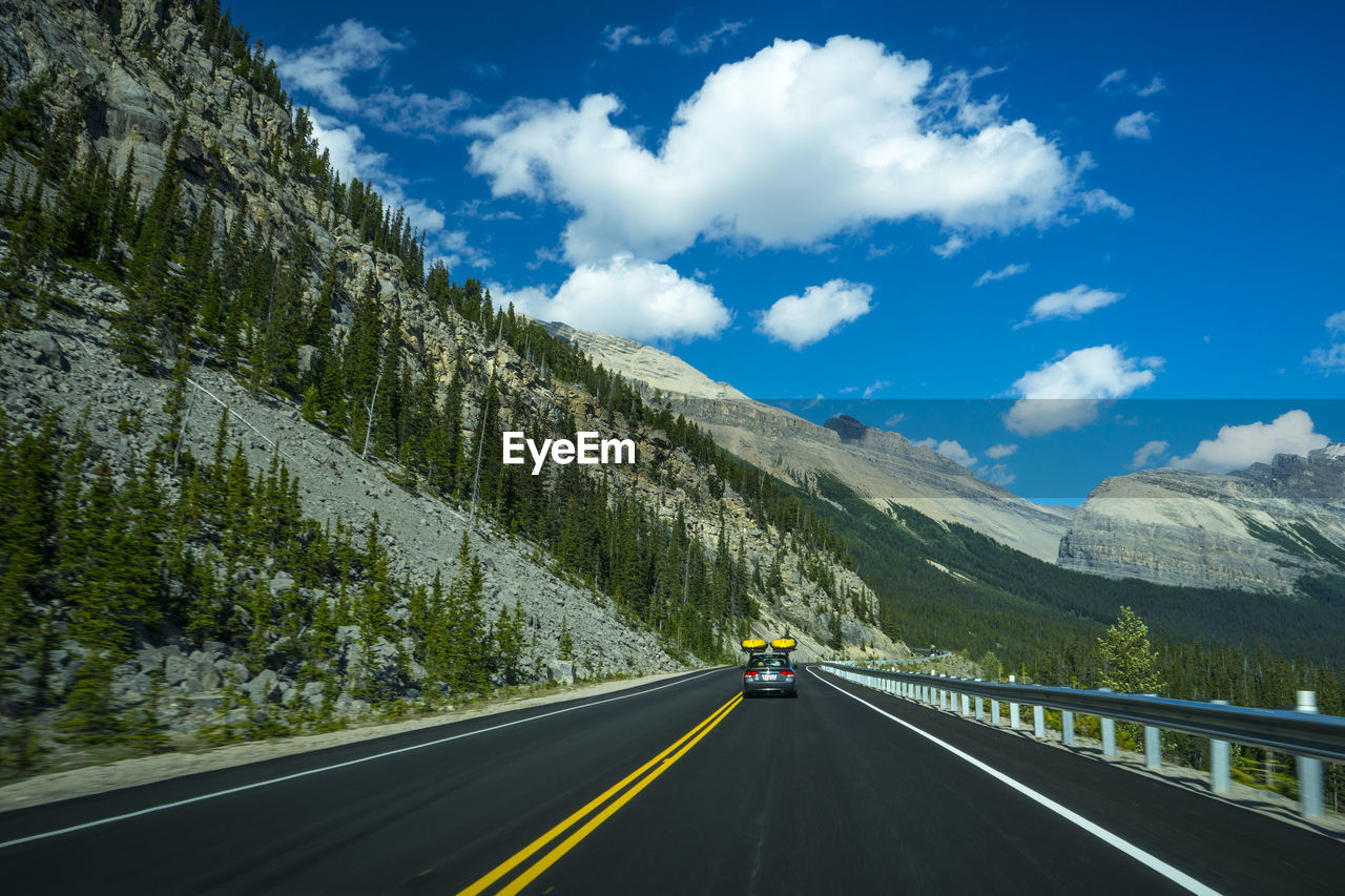 Road with yellow line by mountain against sky and car with yellow cayaks in canada.