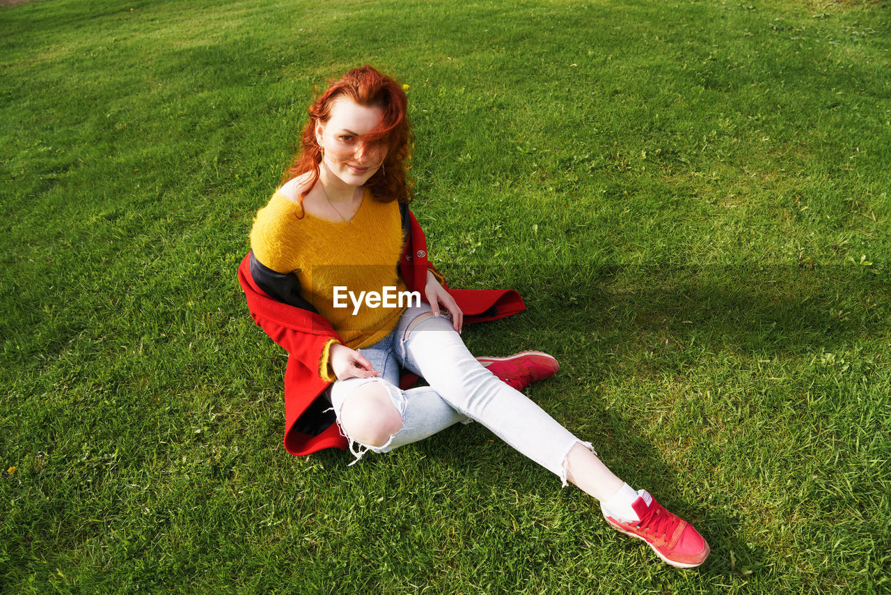 full length of young woman sitting on grassy field