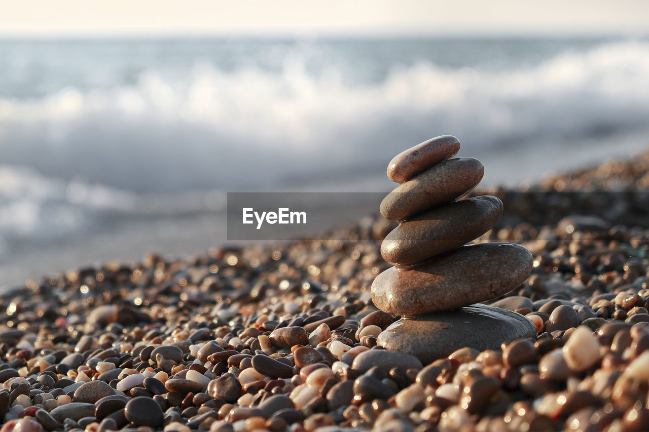 pebble, sand, rock, stone, beach, land, nature, sea, water, shore, close-up, no people, tranquility, large group of objects, selective focus, coast, zen-like, beauty in nature, day, outdoors, sky, abundance, tranquil scene, focus on foreground, water's edge, sunlight, scenics - nature