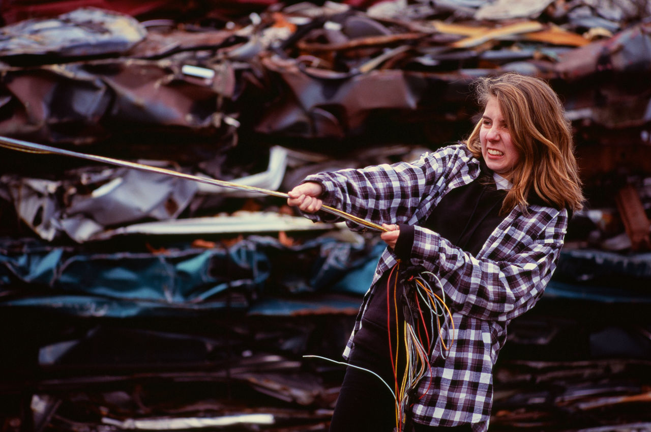 Young woman pulling on wires in an auto salvage yard
