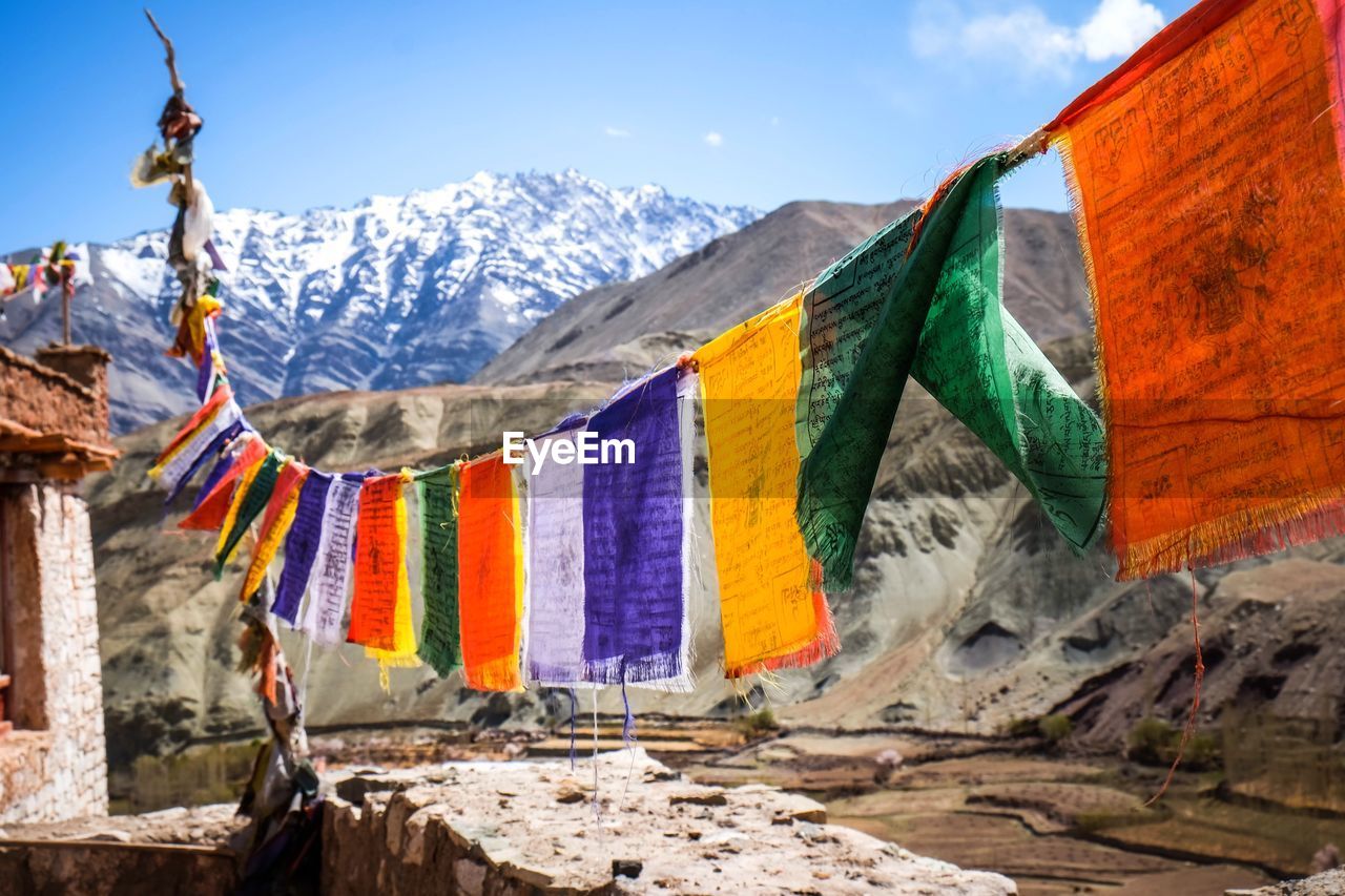 Multi colored flags hanging on mountain against sky