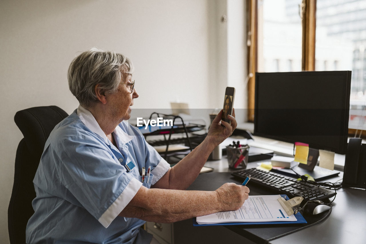 Senior medical expert consulting patient through video call while writing prescription at desk
