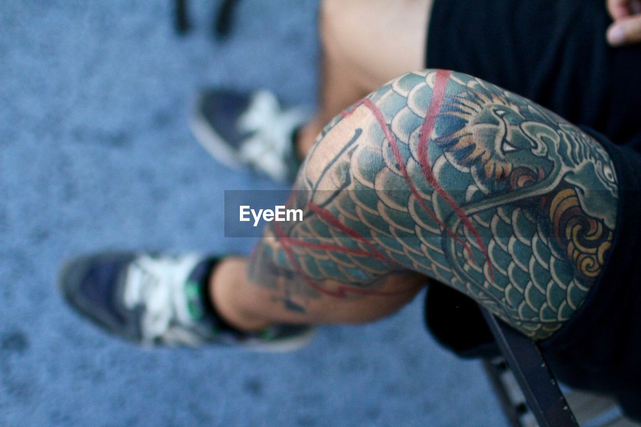 Low section of tattooed man sitting on railing