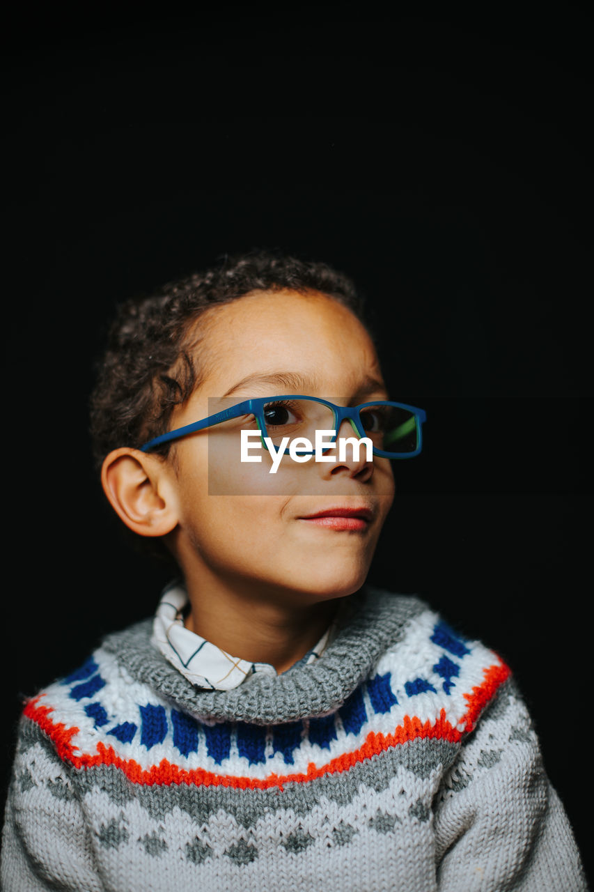 Portrait of boy wearing glasses against black background