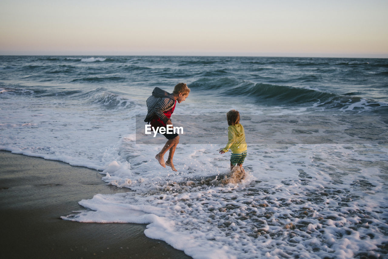 Siblings playing on shore at beach during sunset
