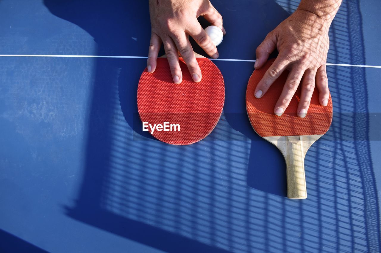 Cropped image of hands with tennis rackets and ball on table