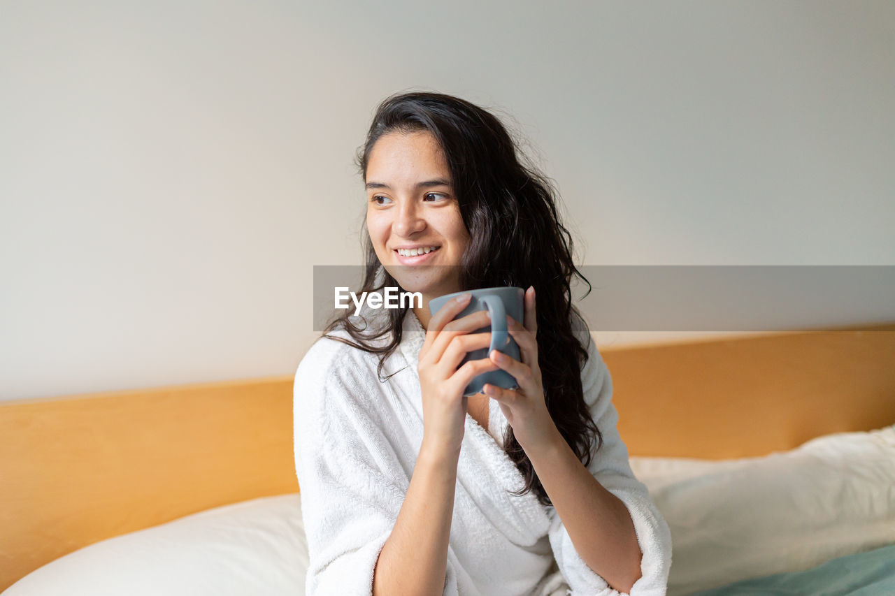 Young woman drinking coffee in bed in bathrobe