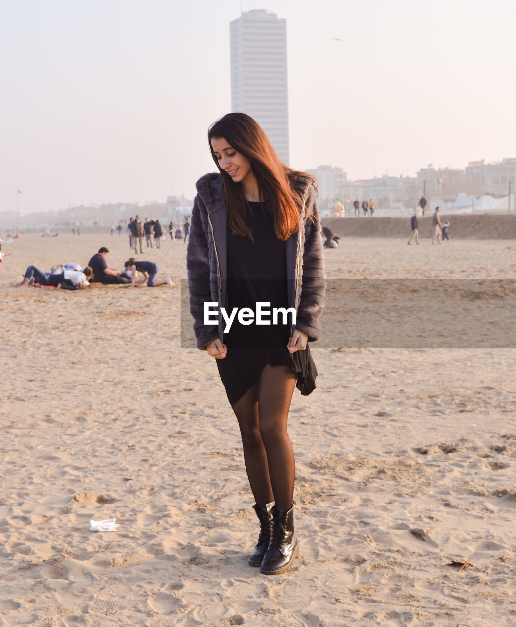 Full length of young woman wearing jacket while standing at sandy beach