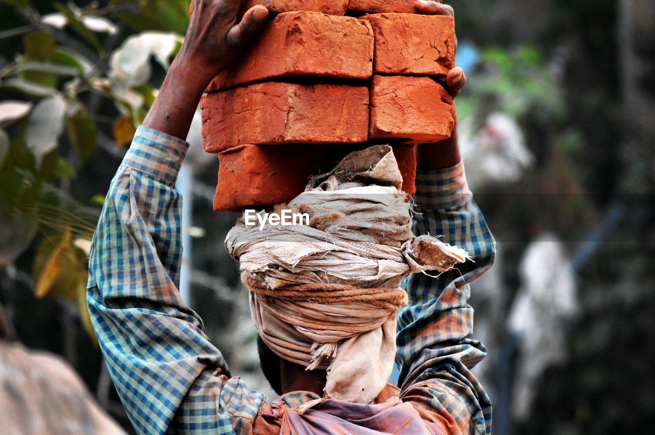 Rear view of worker carrying bricks at construction site
