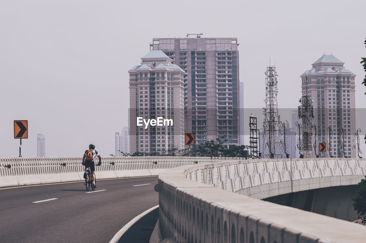 Rear view of man riding bicycle on bridge in city