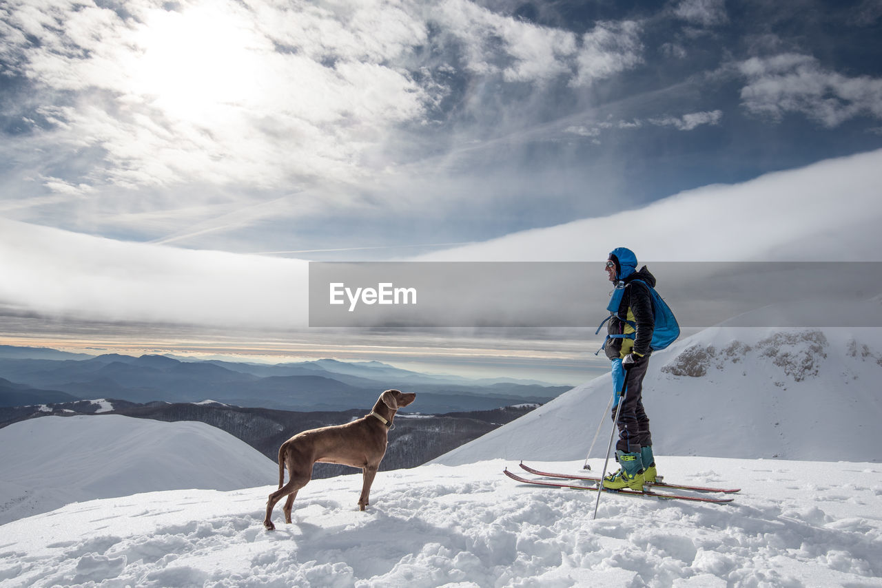Man with dog snowboarding on snowcapped mountain against sky