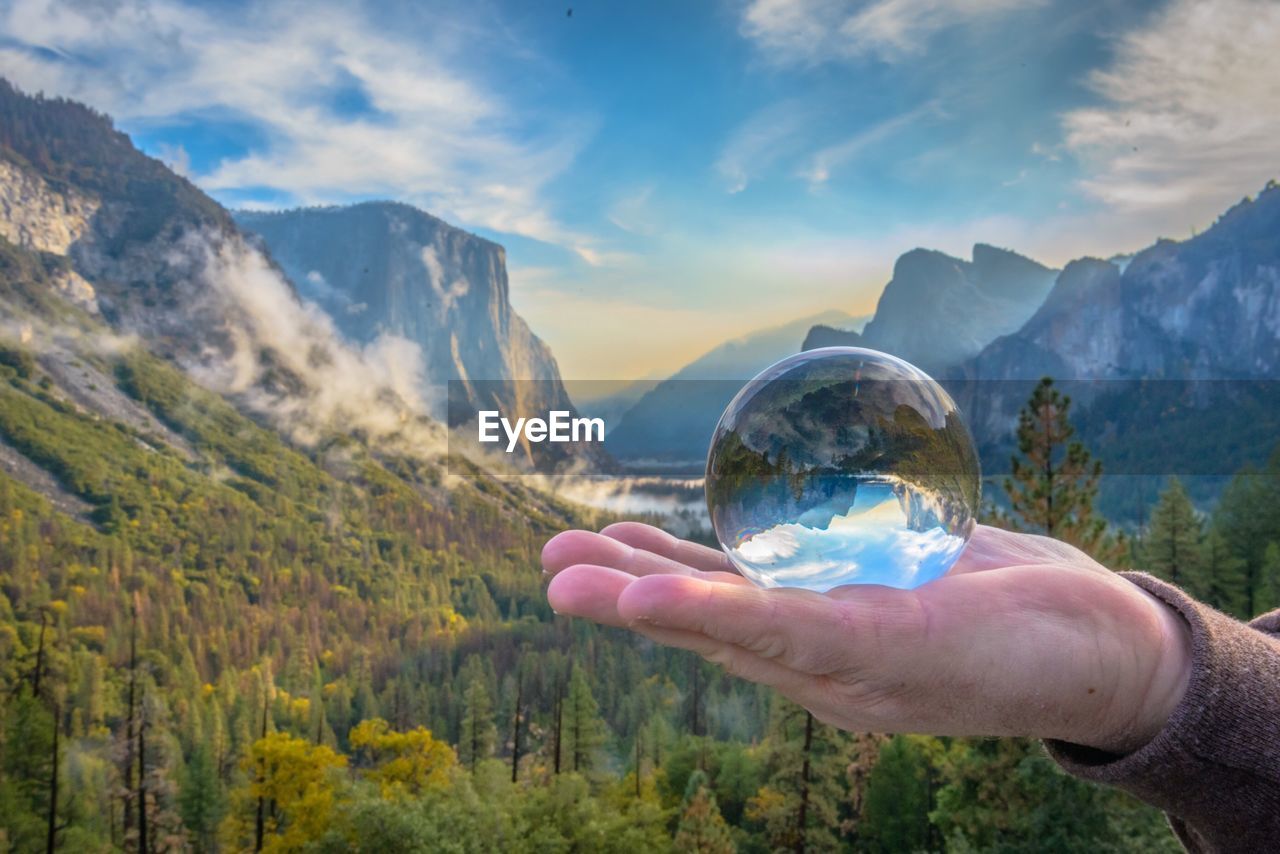 Cropped hand holding crystal ball against mountains
