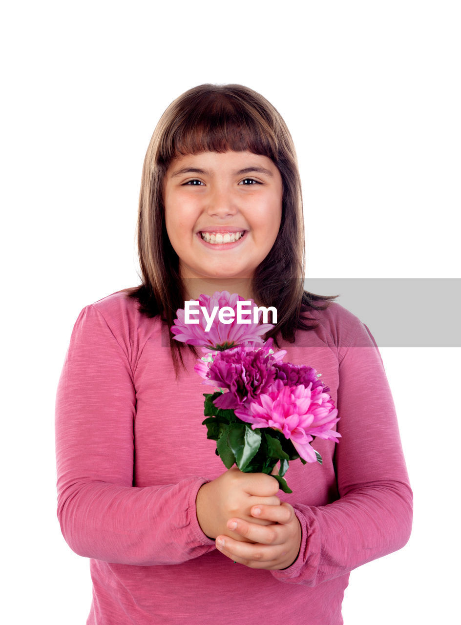 PORTRAIT OF A SMILING YOUNG WOMAN WITH PINK FLOWER AGAINST WHITE BACKGROUND